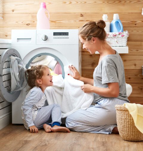 Çamaşır makinesine kıyafet koyan kadın ve kızı